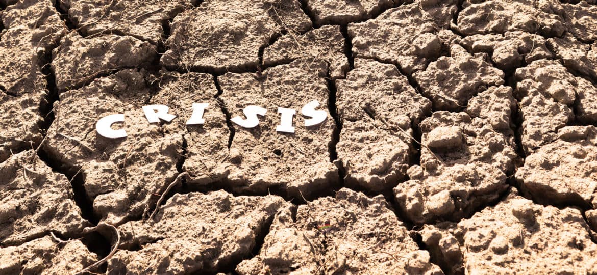 The word CRISIS in paper letters on the background of dry earth with cracks. Crisis concept. Banner.