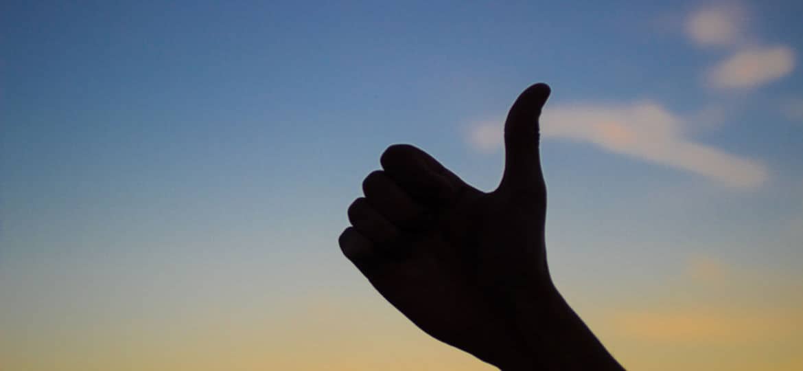 Silhouette of hand with thumbs up, symbol of like, satisfaction and agreement, sky background